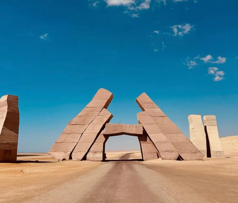 The massive stone structure of Allah's Gate spanning a desert road in Ras Mohammed National Park, Sharm El Sheikh, under a bright blue sky.
